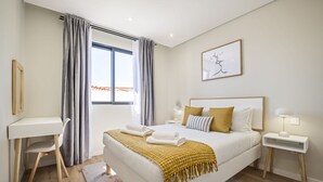 A modern bedroom with a large bed, a desk, and a window with curtains. - Casa da Oliveira III by Homie (Santa Cruz)