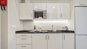 A modern kitchen with white cabinets, a built-in microwave, a stainless steel refrigerator, and a countertop with a wine bottle and coffee maker.