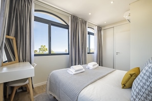 A modern hotel room with a large window, a desk, and a neatly made bed.