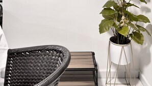 Et hjørne med en fletstol, en potteplante og en dekorativ vægdekoration.
