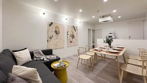 A modern living room with a grey sofa, a yellow side table, and a dining area with wooden chairs and a table set for four. - Nikke 202 (Hiroshima)