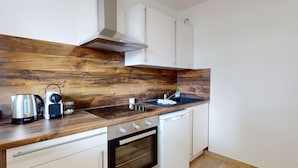 A compact kitchen with a wooden backsplash, a stove, a sink, and white cabinetry. - Brasseur (Colmar)