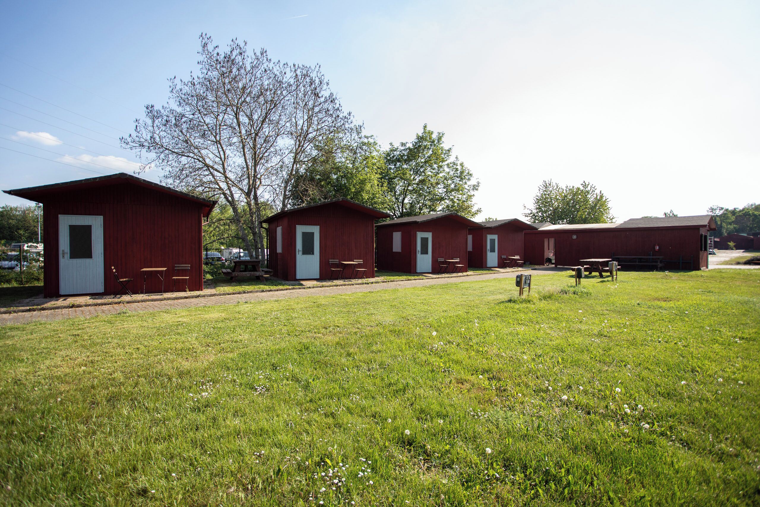 A row of red cabins with white doors, each with a small table and chair outside.