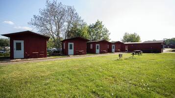 A row of red cabins with white doors, each with a small table and chair outside.