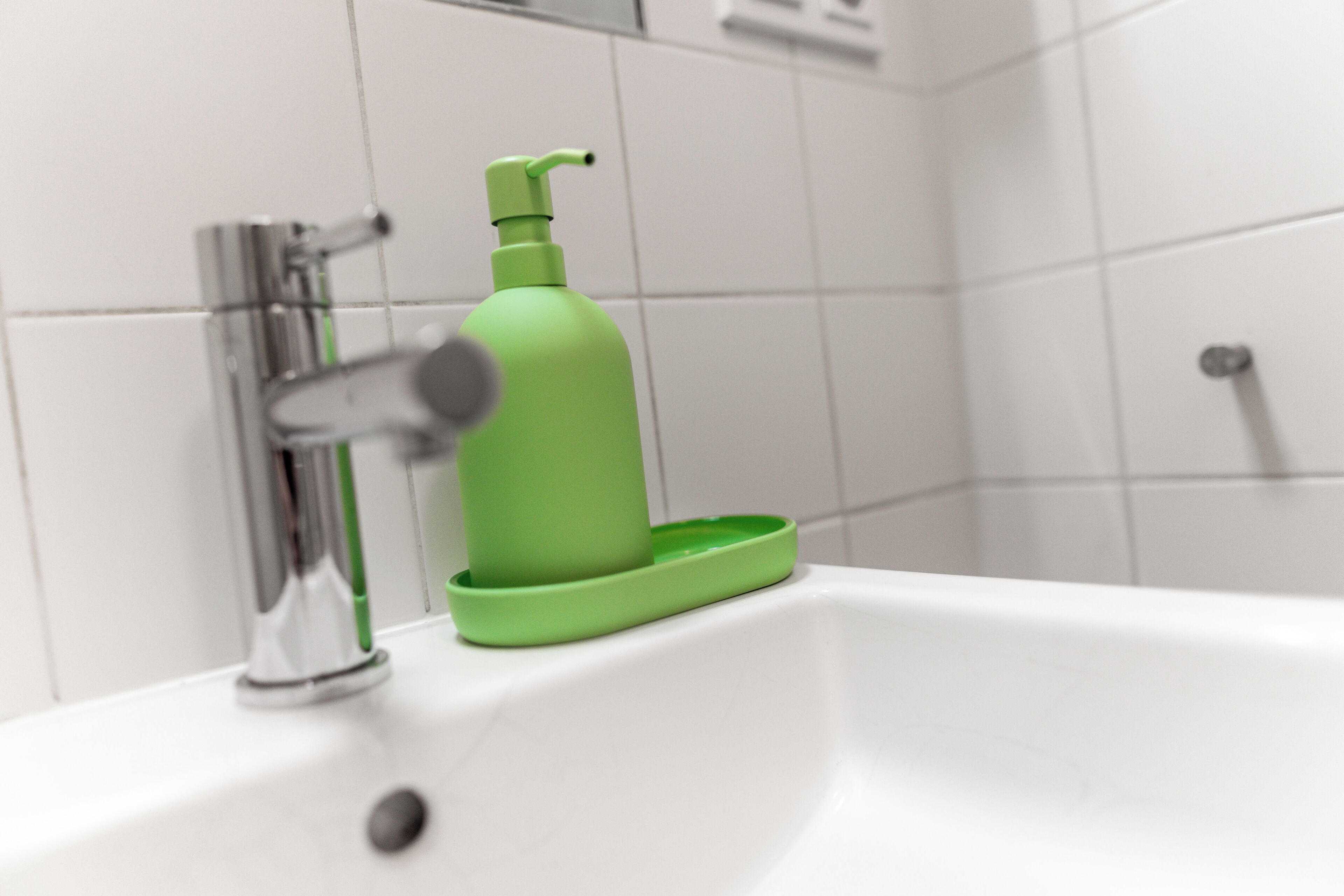 A bathroom sink with a green soap dispenser and a chrome faucet.