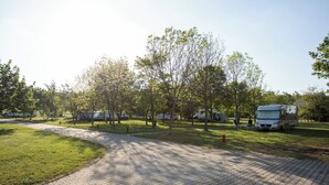 A paved walkway leading to RVs and trailers, surrounded by trees and grass. - Camp Dzban (Prague)