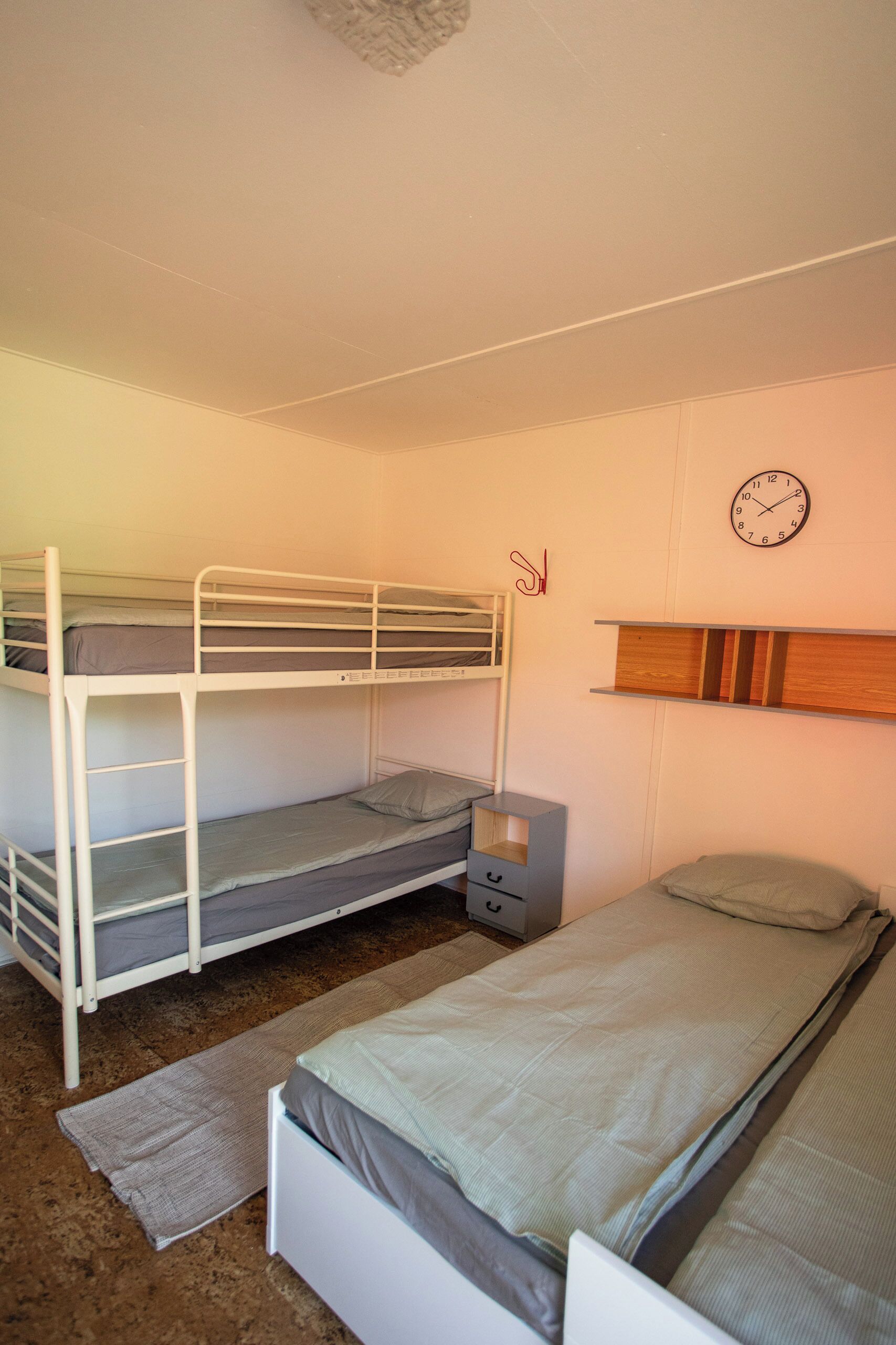 Une chambre avec un lit superposé, une tête de lit en bois, une table de chevet et une horloge murale.