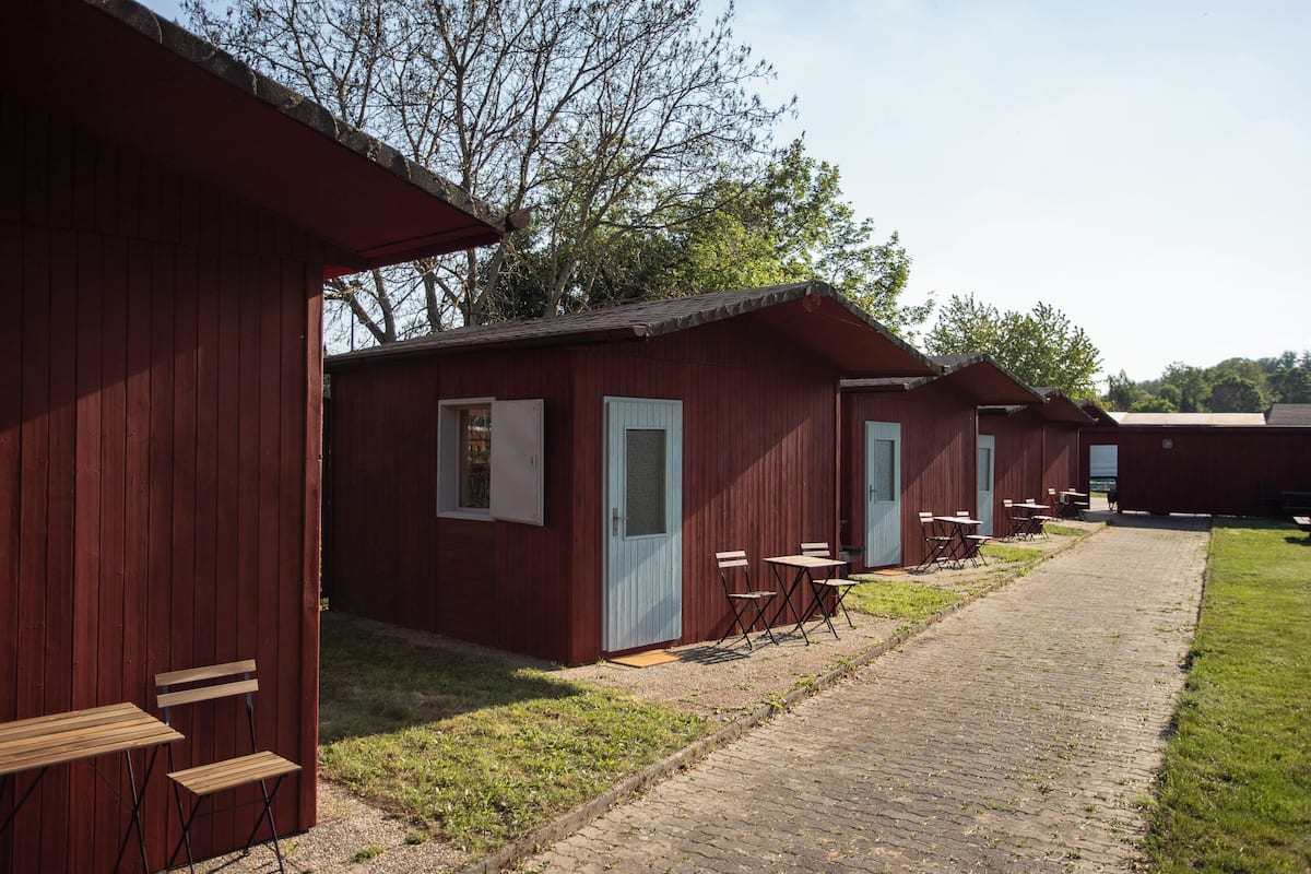 A row of red wooden cabins with outdoor seating areas and a paved walkway.