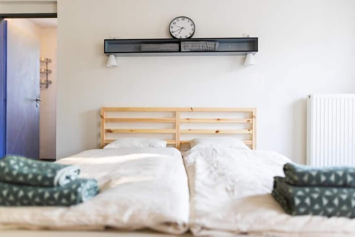 A bedroom with a wooden headboard, a wall-mounted clock, and a shelf with two lamps.