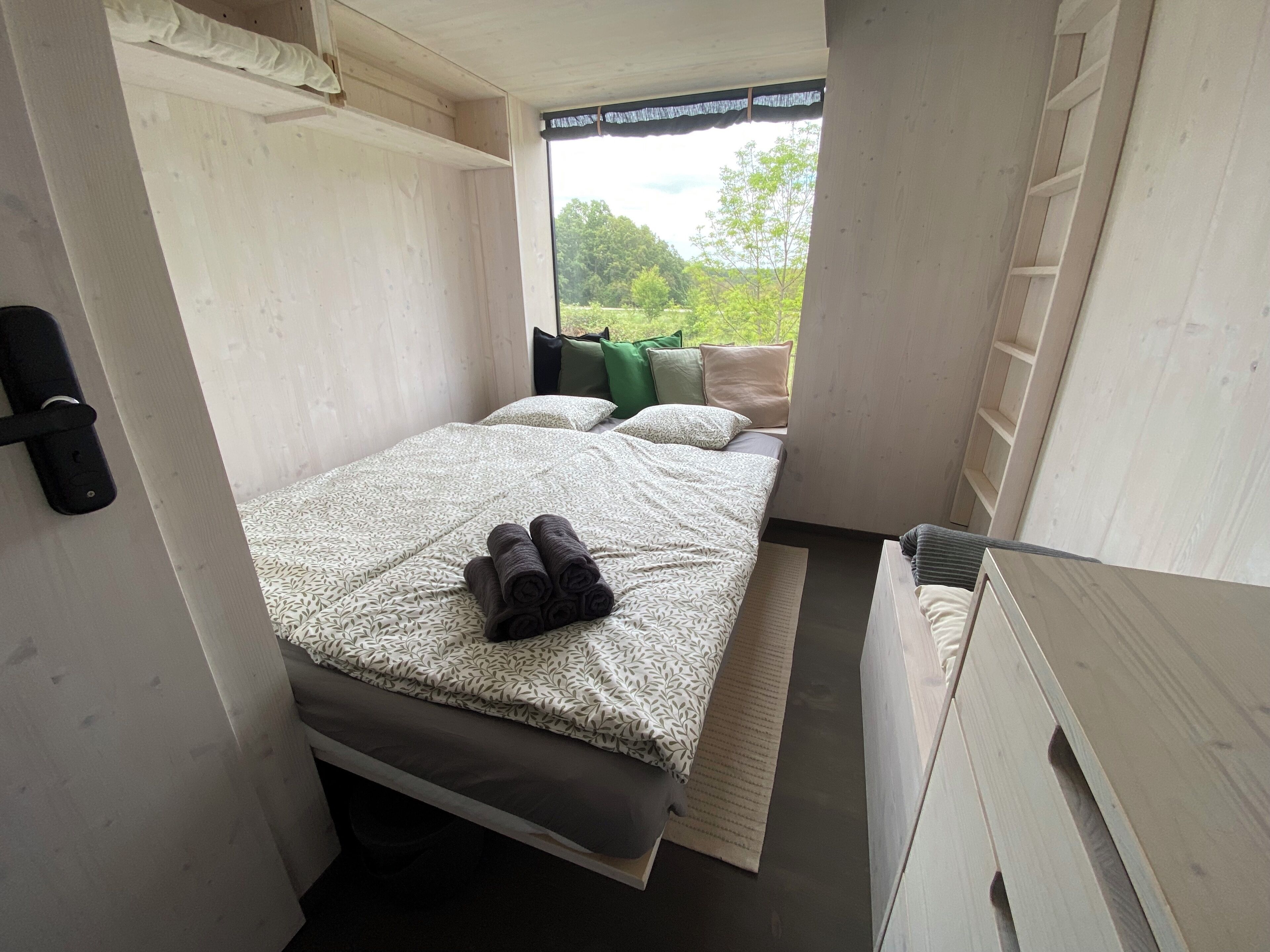A compact bedroom with a bed, pillows, and a view of greenery outside.