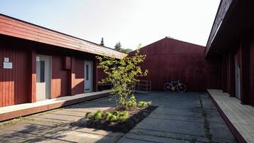 Une cour avec un petit arbre, un vélo et un bâtiment dont le revêtement extérieur est rouge.
