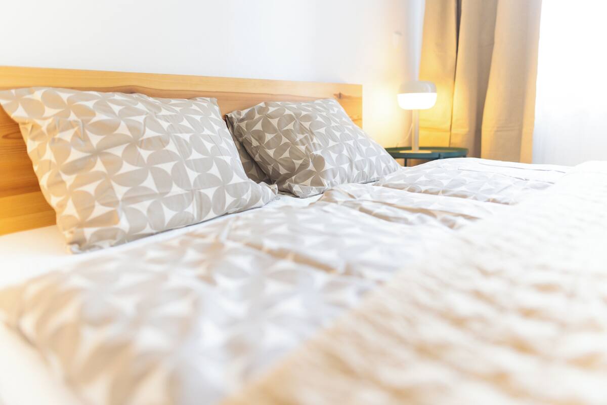 A neatly made bed with patterned pillows, a wooden headboard, and a bedside lamp.