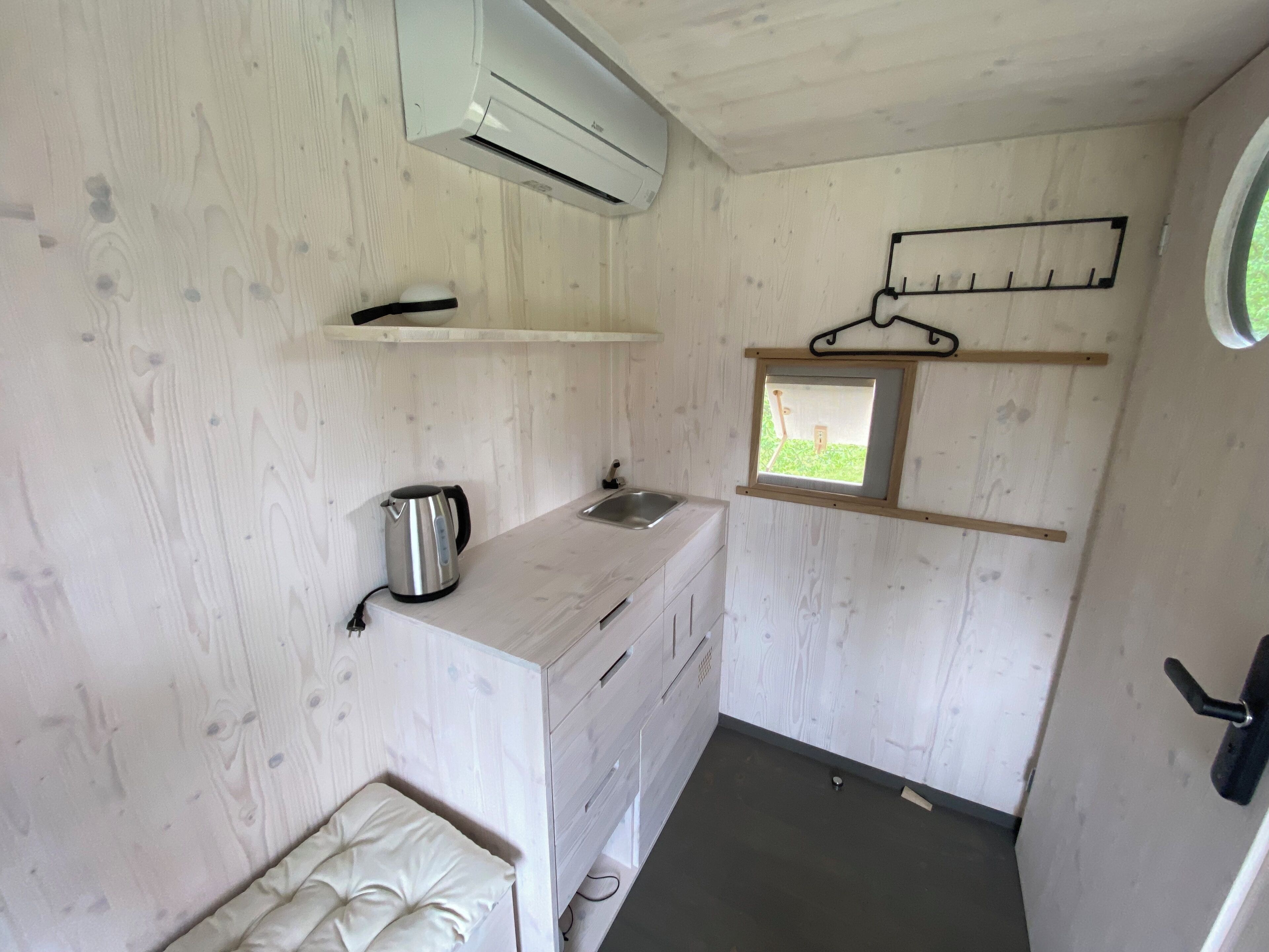 A compact kitchen with a built-in stove, a small window, and a hanging rack.