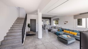 Ein modernes Wohnzimmer mit Treppe, grauen Fliesen, einem grauen Sofa mit gelben Kissen und einem Flachbildfernseher.