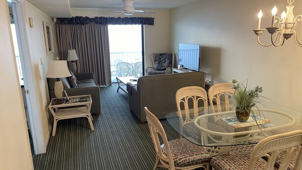 Ein Hotelzimmer mit Essbereich, einer Couch, einem Fernseher und einem Balkon mit Vorhängen.
