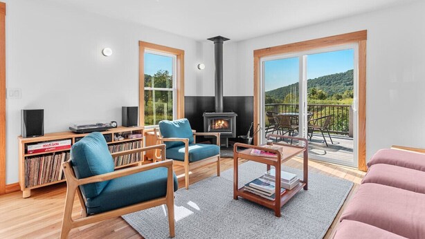 A modern living room with a fireplace, a sofa, a coffee table, and a bookshelf. - Secluded Cottage on 85 Acres – Peaceful Country Retreat Surrounded by Nature (Walton)