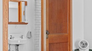 A bedroom with a bed, a wooden door, a bathroom with a sink, and a fan. - Secluded Cottage on 85 Acres – Peaceful Country Retreat Surrounded by Nature (Walton)