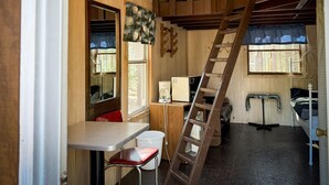 Een compacte kamer met houten lambrisering, voorzien van een stapelbed, een ladder, een bureau en een stoel.