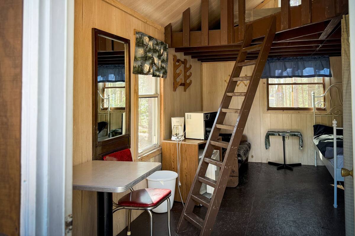 Een compacte kamer met houten lambrisering, voorzien van een stapelbed, een ladder, een bureau en een stoel.