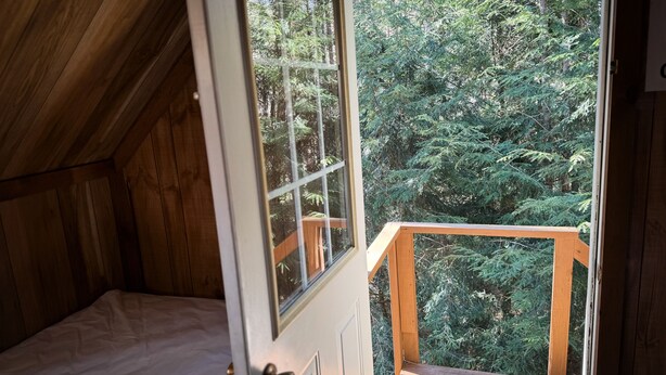 Een slaapkamer met een houten plafond en een groot raam met uitzicht op een bos.