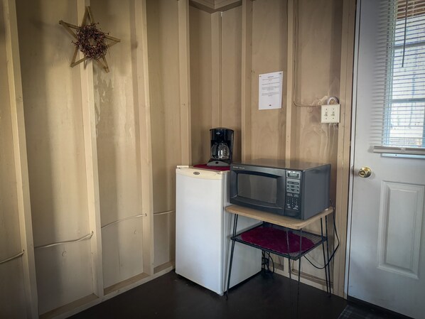 Cocina compacta con refrigerador, microondas sobre un pedestal metálico y cafetera sobre el refrigerador.