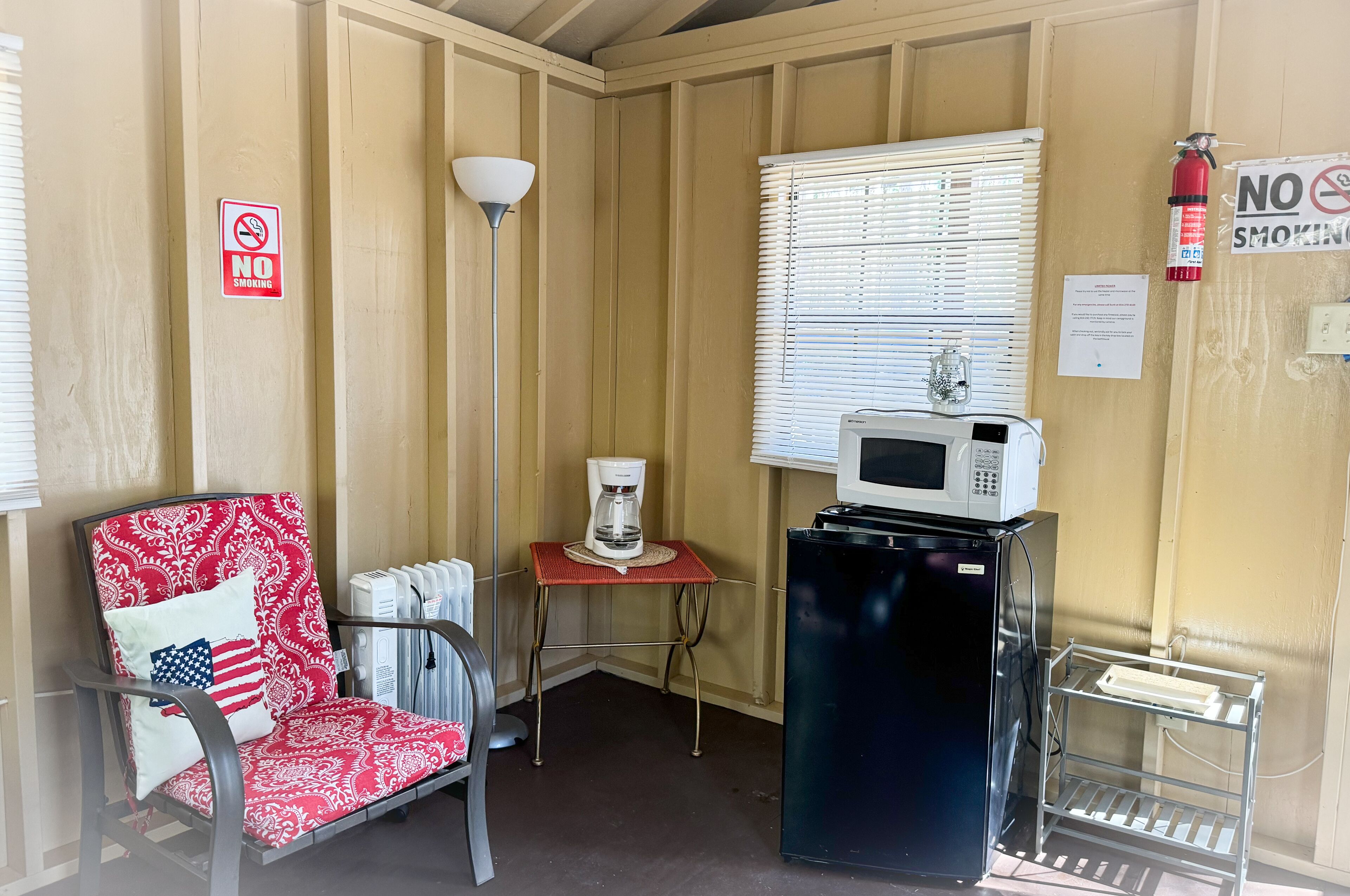 Una habitación pequeña con una silla, cafetera, microondas y refrigerador.
