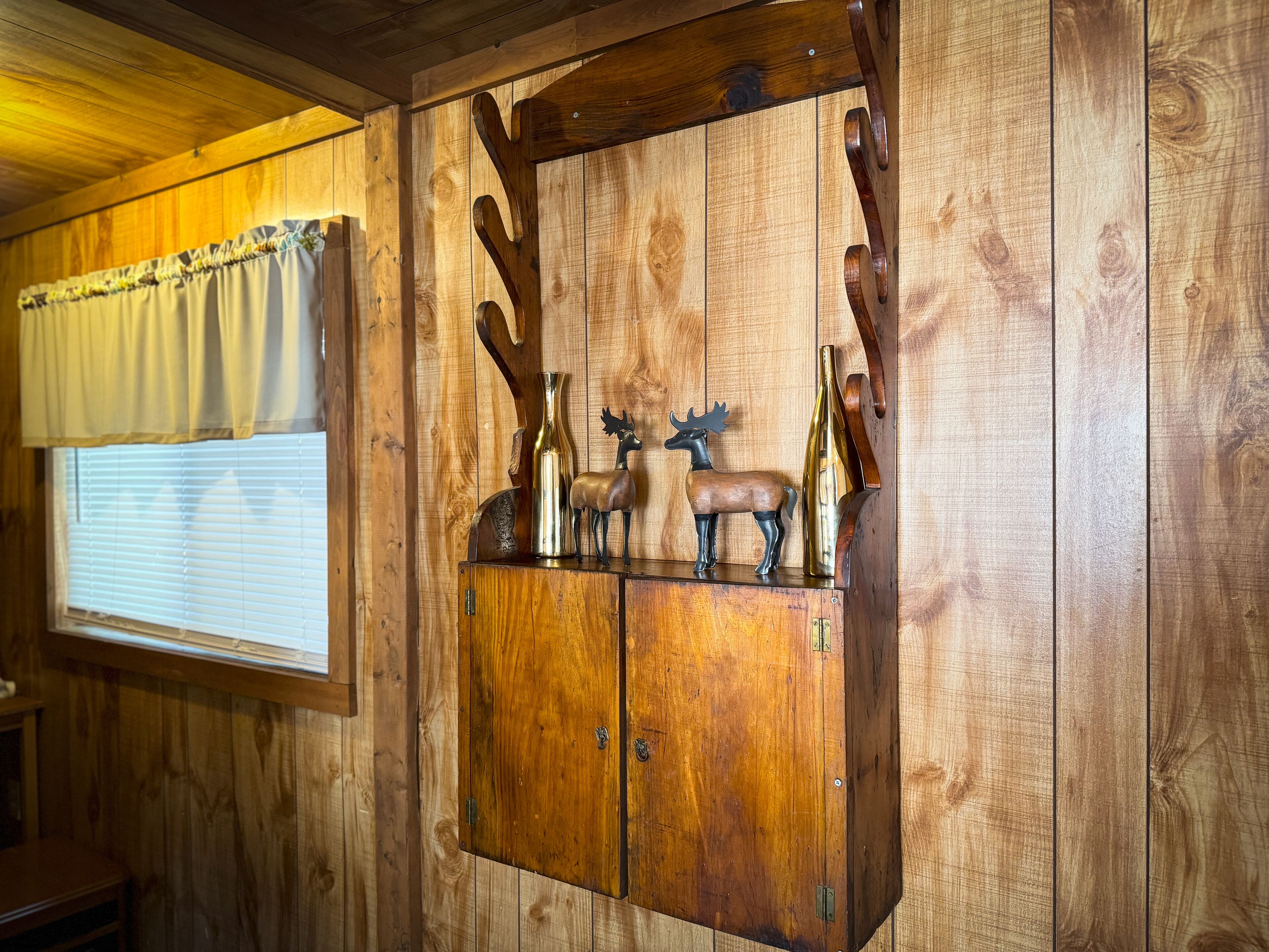 Un meuble en bois surmonté d’une fenêtre, décoré d’un cerf en métal et d’un vase.