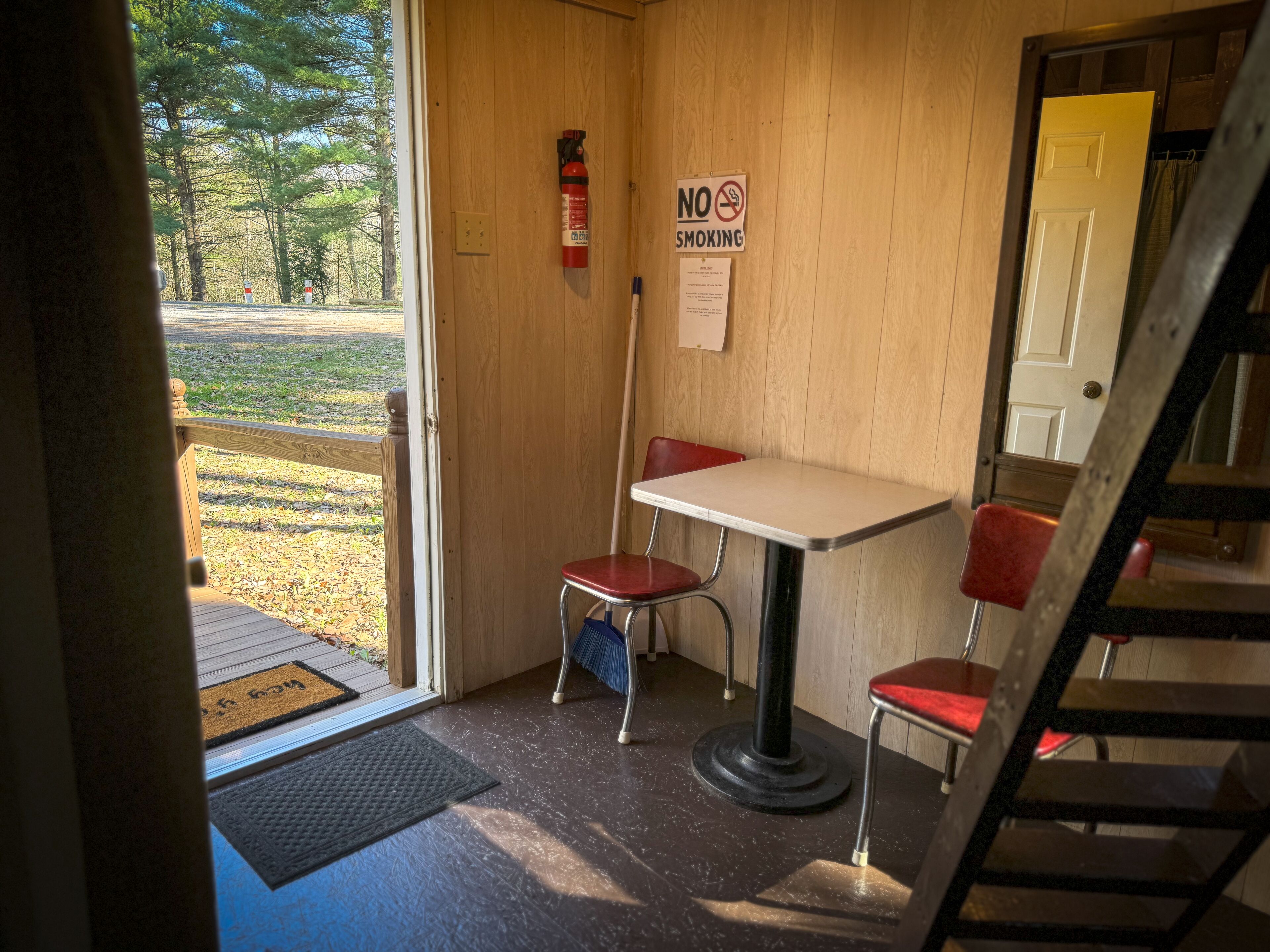 Un petit espace de restauration clos, avec un intérieur en bois, une table, deux chaises rouges, un extincteur et un panneau indiquant « Il est interdit de fumer ».