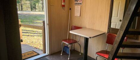 Un petit espace de restauration clos, avec un intérieur en bois, une table, deux chaises rouges, un extincteur et un panneau indiquant « Il est interdit de fumer ».