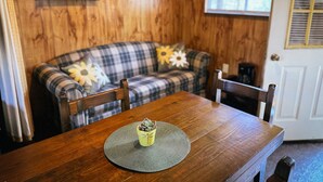 Een houten interieur met een geruit bankje, een eettafel met placemat en een kleine plant in een pot.