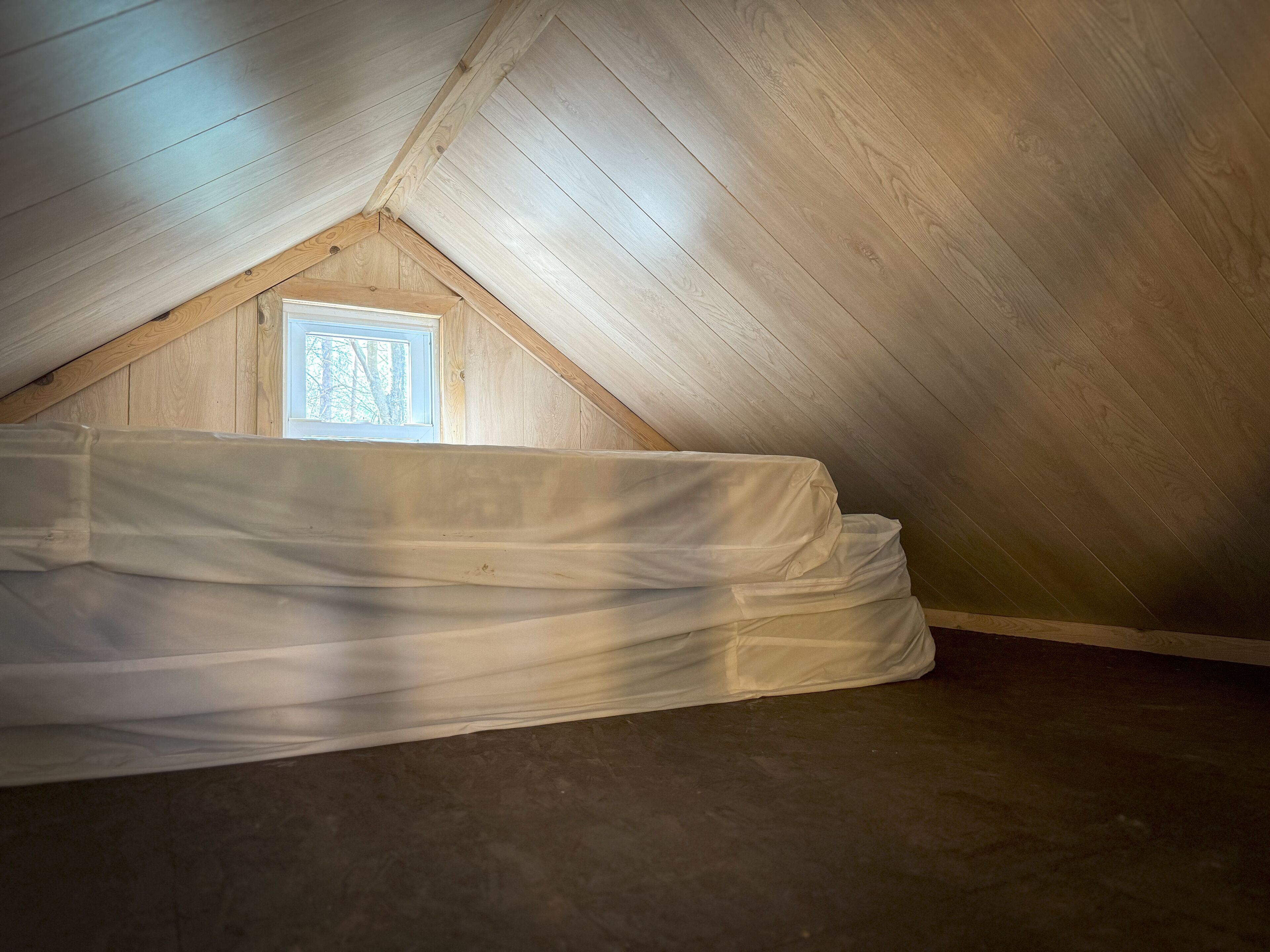 Habitación en ático con vigas de madera, tragaluz y un colchón.