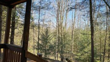A wooden deck with a bench and a table, overlooking a forested area with tall trees.