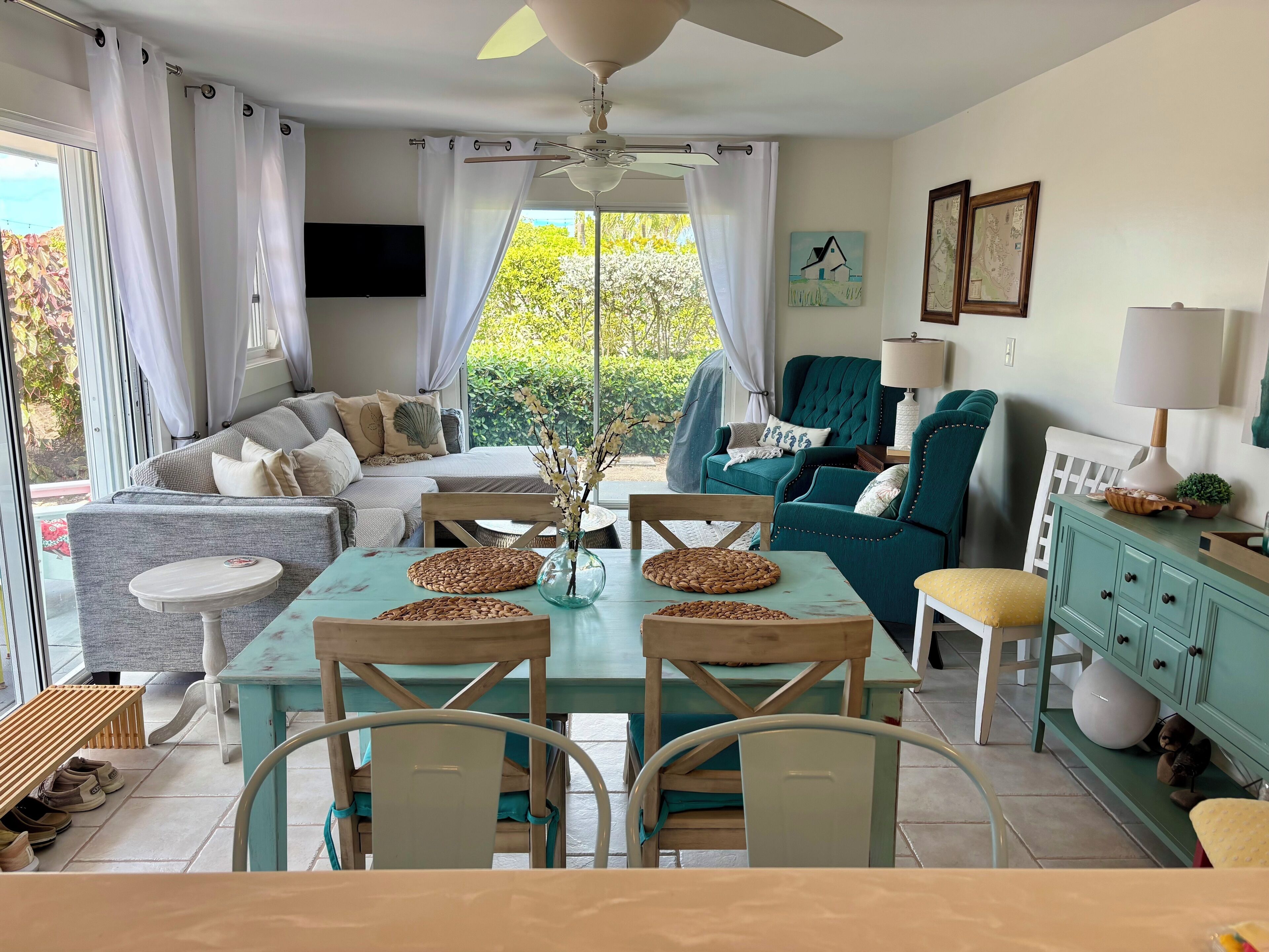 Un salon bien éclairé, avec un canapé, des fauteuils, une table à manger et un ventilateur de plafond.