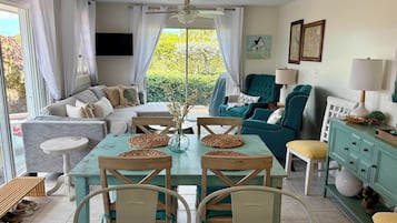 Un salon bien éclairé, avec un canapé, des fauteuils, une table à manger et un ventilateur de plafond.