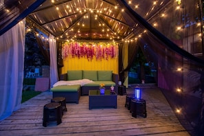An outdoor seating area with a green sofa, two side tables, and string lights.