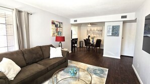 A living room with a brown sofa, a glass coffee table, and a dining area with a table and chairs. - Tempe 2Bdrm 2Ba by Papago Park A101 (Tempe)