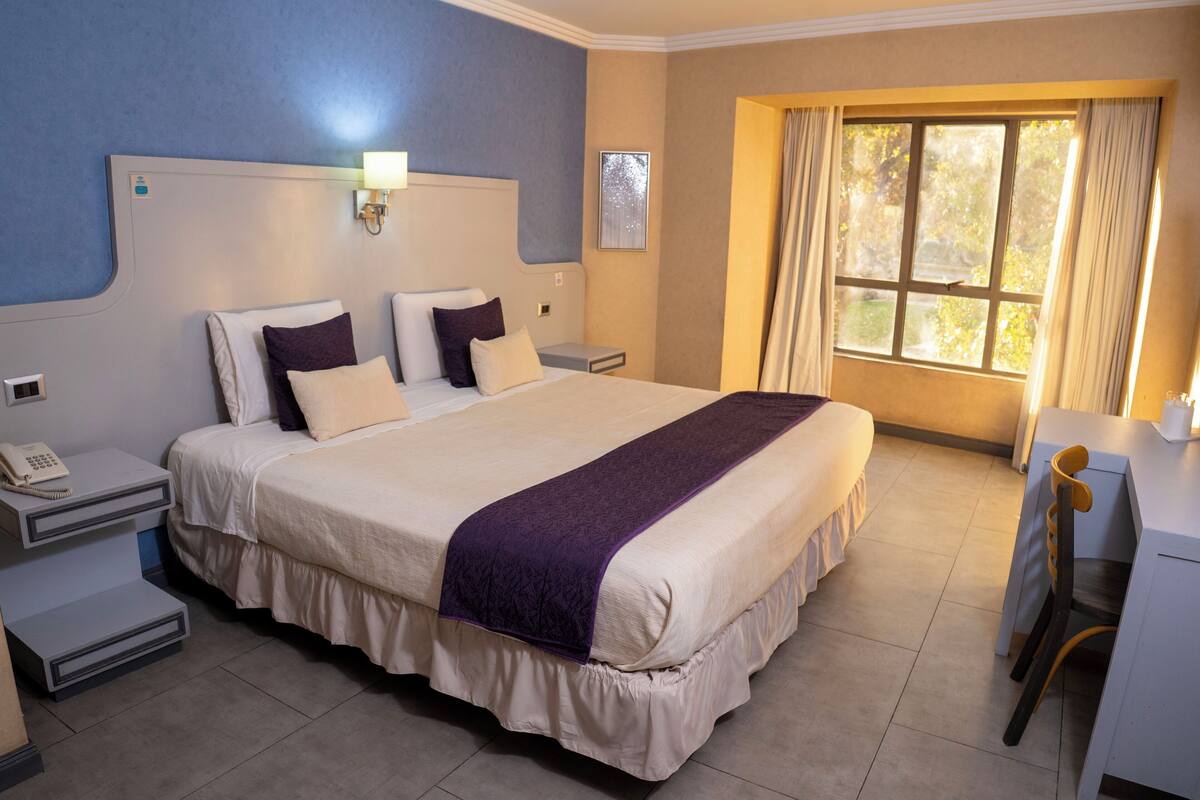 A hotel room with a large bed, bedside tables, a desk, and a window with curtains.