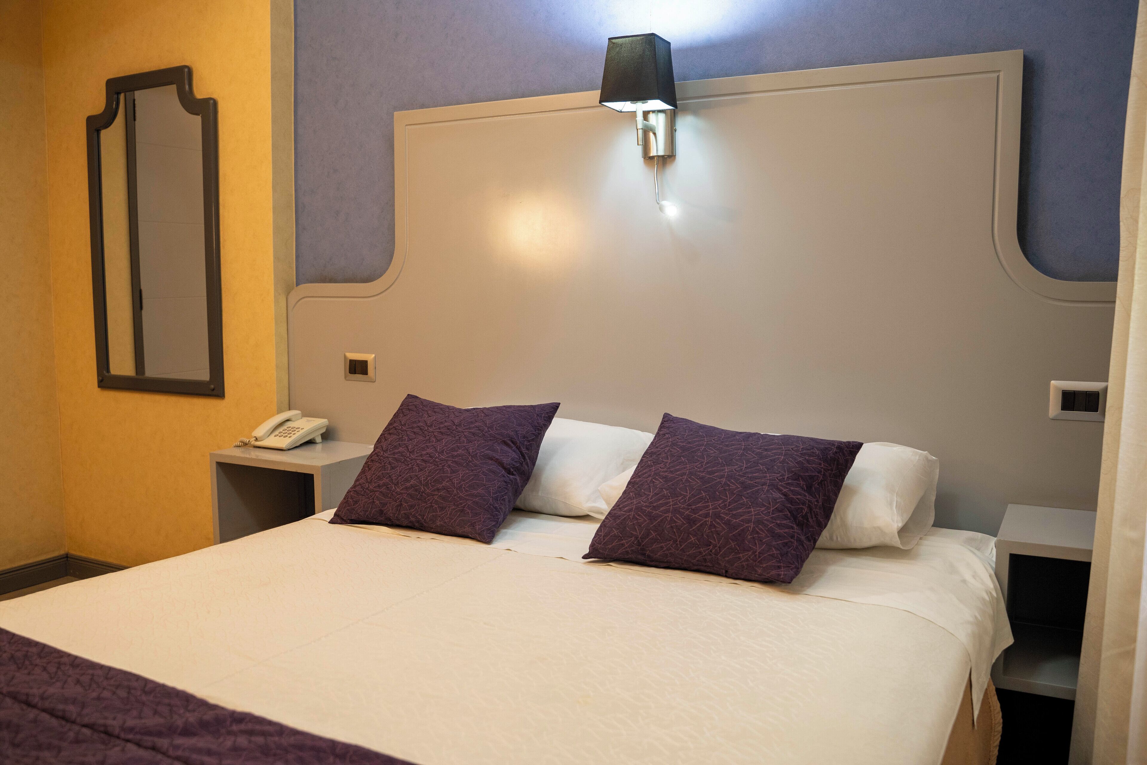 A hotel room with a large bed, two pillows, a bedside table with a lamp, and a phone.
