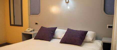 A hotel room with a large bed, two pillows, a bedside table with a lamp, and a phone.
