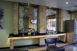 Uma área de recepção com balcão de mármore, televisão na parede e um frigorífico à direita.