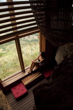 A room with a large window, a wooden bench, and a red cushion.