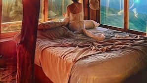 A room with a large bed, a hanging mosquito net, and a view of a mountainous landscape through large windows. - Refugio La Roca  (Los Santos)