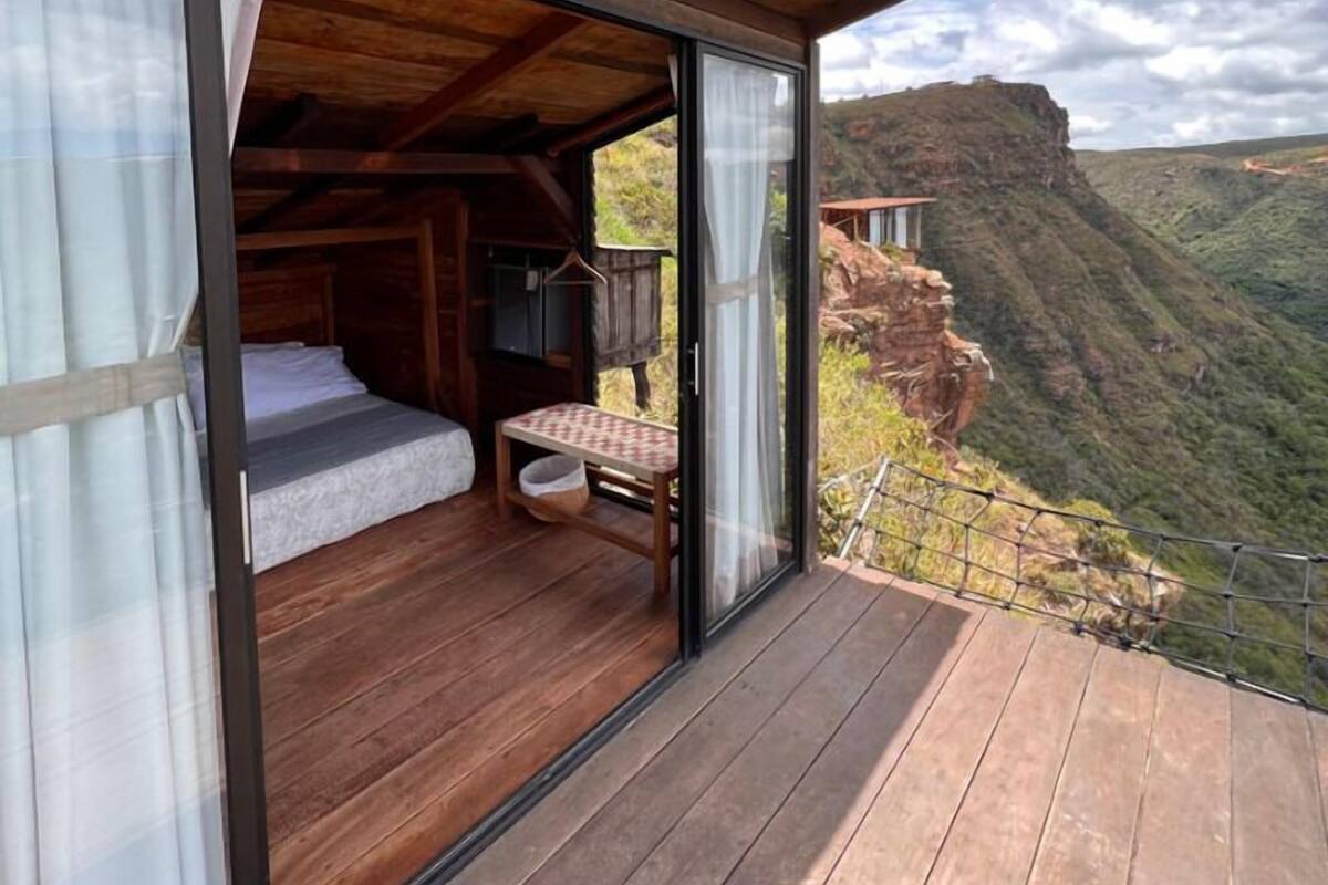 A wooden cabin with a large glass door leading to a bedroom with a bed and a small table.