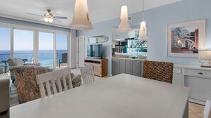 Une cuisine moderne dotée d’un grand îlot central, d’un coin repas avec une table blanche et d’une vue sur l’océan.