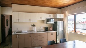 Cocina compacta con techo de madera, microondas, refrigerador y comedor con mesa y sillas.