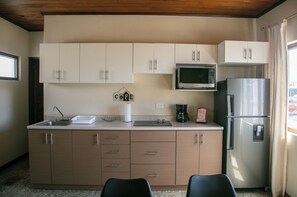A compact kitchen with a microwave, refrigerator, and a sink. There are cabinets and a countertop with a few items on it.