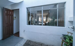 Eine weiße Außenwand mit einem großen Fenster, einer Holztür und einer kleinen Stufe zum Eingang.