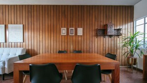 Une salle de conférence avec une table et des chaises en bois, un canapé, des tableaux encadrés et une plante en pot.