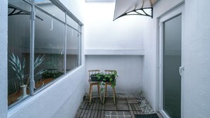 Un petit espace patio avec une chaise en bois et des plantes en pot, un mur blanc et une porte-fenêtre coulissante.