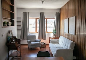 En stue med sofa, lænestol, træhylder og et lille bord.